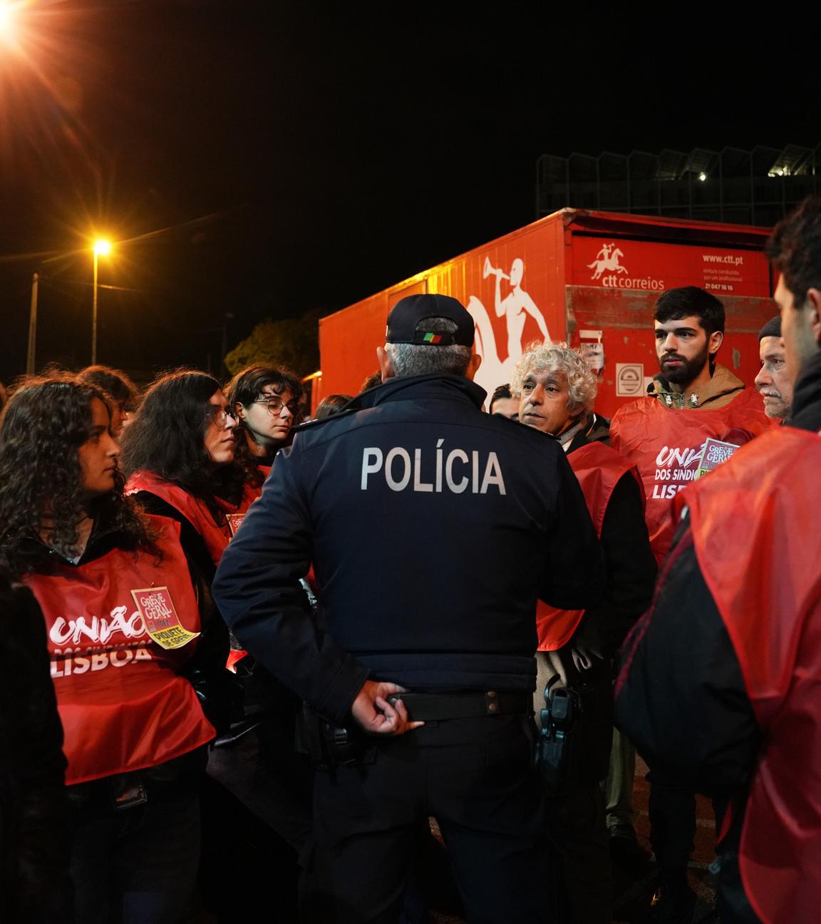 Polizist verhandelt mit streikenden Arbeitern an Postlager in Lissabon während Generalstreik gegen Arbeitsrechtsreformen.