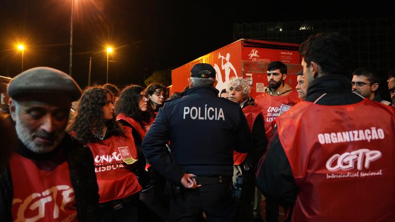 Polizist verhandelt mit streikenden Arbeitern an Postlager in Lissabon während Generalstreik gegen Arbeitsrechtsreformen.