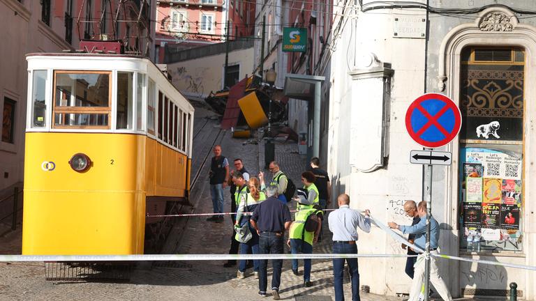 Eine abgesperrte Fläche mit der kaputten Standsteilbahn in Lissabon. Um herum mehrere Menschen mit Warnwesten, vermutlich Polizisten oder Sicherheitsdienst-Personal