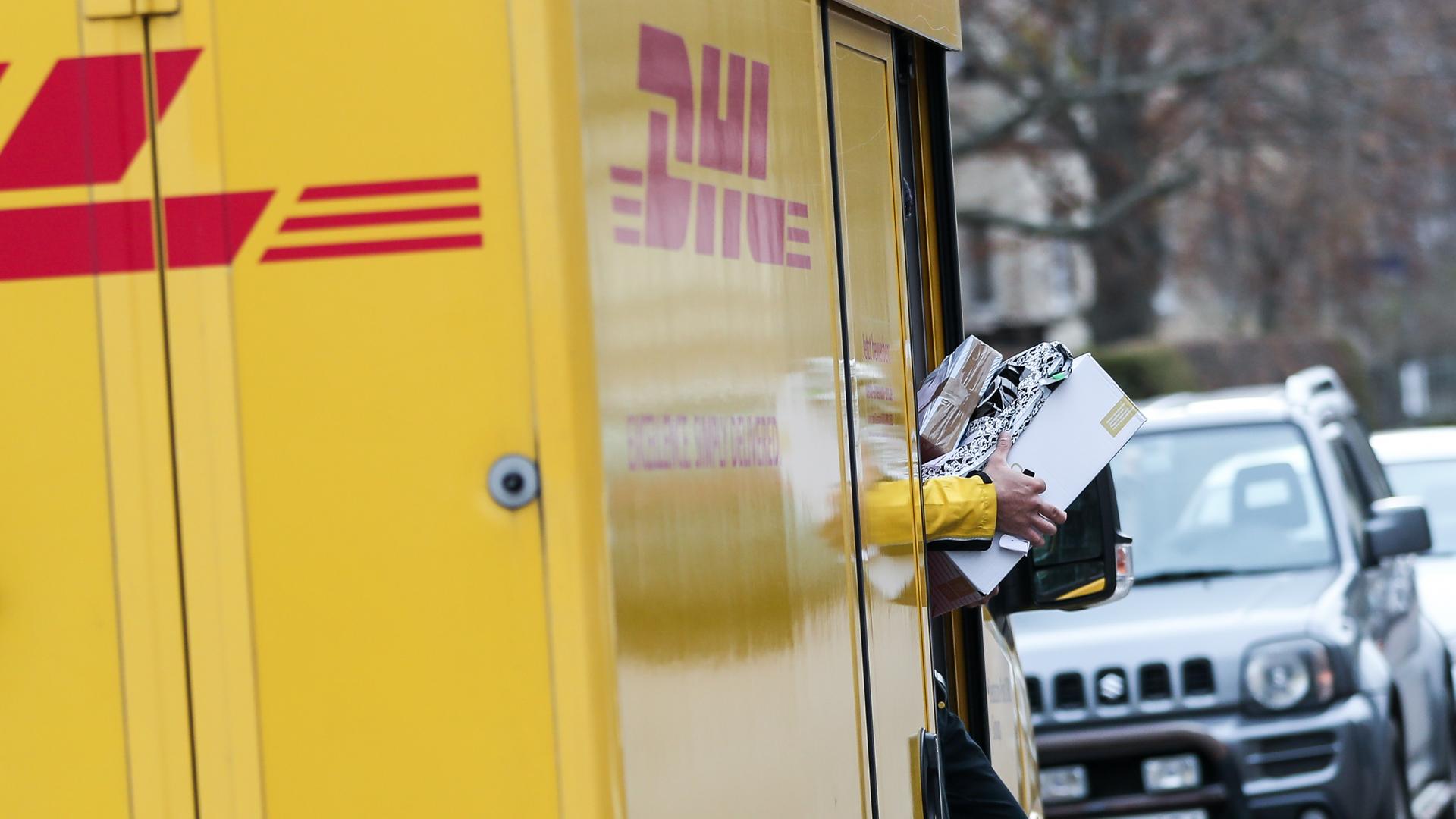 Ein DHL Paketzusteller verlässt mit mehreren Sendungen sein Fahrzeug.