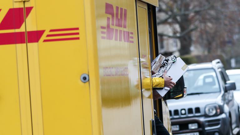 Ein DHL Paketzusteller verlässt mit mehreren Sendungen sein Fahrzeug.