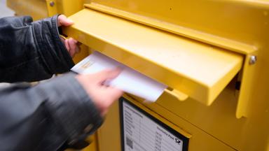 Eine Person wirft einen frankierten Brief in einen Briefkasten.