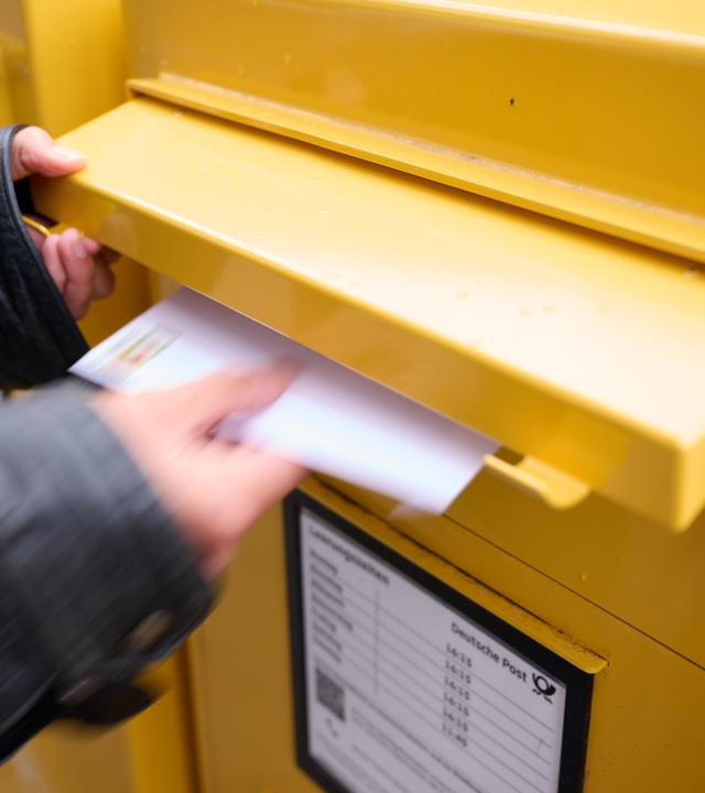 Eine Person wirft einen frankierten Brief in einen Briefkasten.