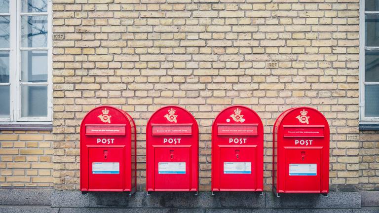 vier rote Briefkästen der dänischen Post an einer Hauswand in Aarhus.