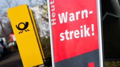  Ein Aufsteller mit der Aufschrift "Heute Warnstreik!"  steht neben einem Briefkasten der Deutschen Post. 