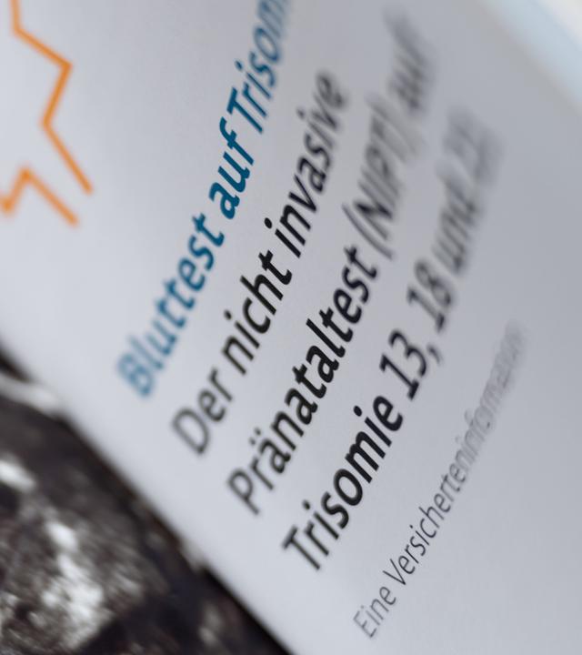 Zwei Informationsbroschüren zu nicht-invasiven Pränataltests liegen neben einem Ultraschallbild in einer Frauenarztpraxis. (Archiv)