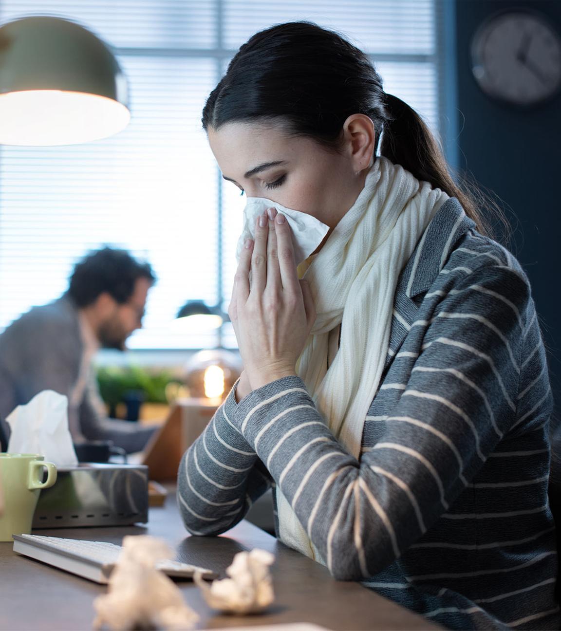 Junge Frau schnäuzt im Büro die Nase