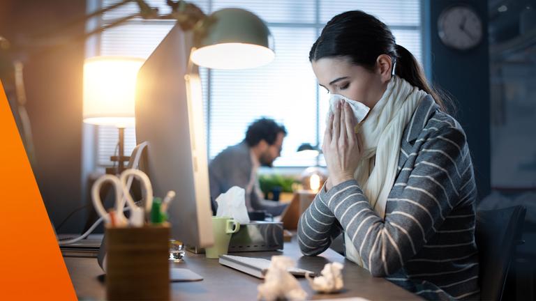 Junge Frau schnäuzt im Büro die Nase