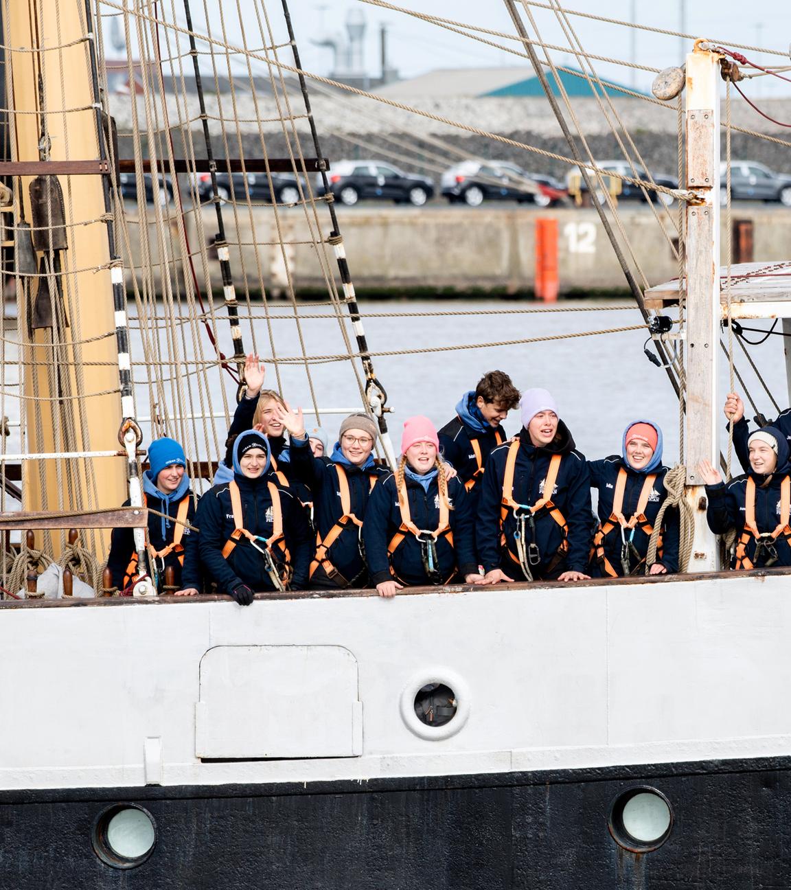 Schülerinnen und Schüler begrüßen bei der Einfahrt in den Hafen von Bord des Schulschiffs "Pelican of London" ihre an Land wartenden Angehörigen am 10.04.2021, Niedersachsen, Emden.