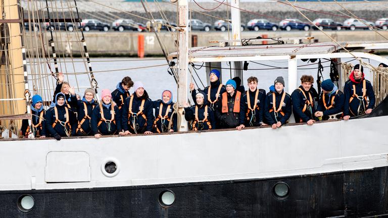 Schülerinnen und Schüler begrüßen bei der Einfahrt in den Hafen von Bord des Schulschiffs "Pelican of London" ihre an Land wartenden Angehörigen am 10.04.2021, Niedersachsen, Emden.