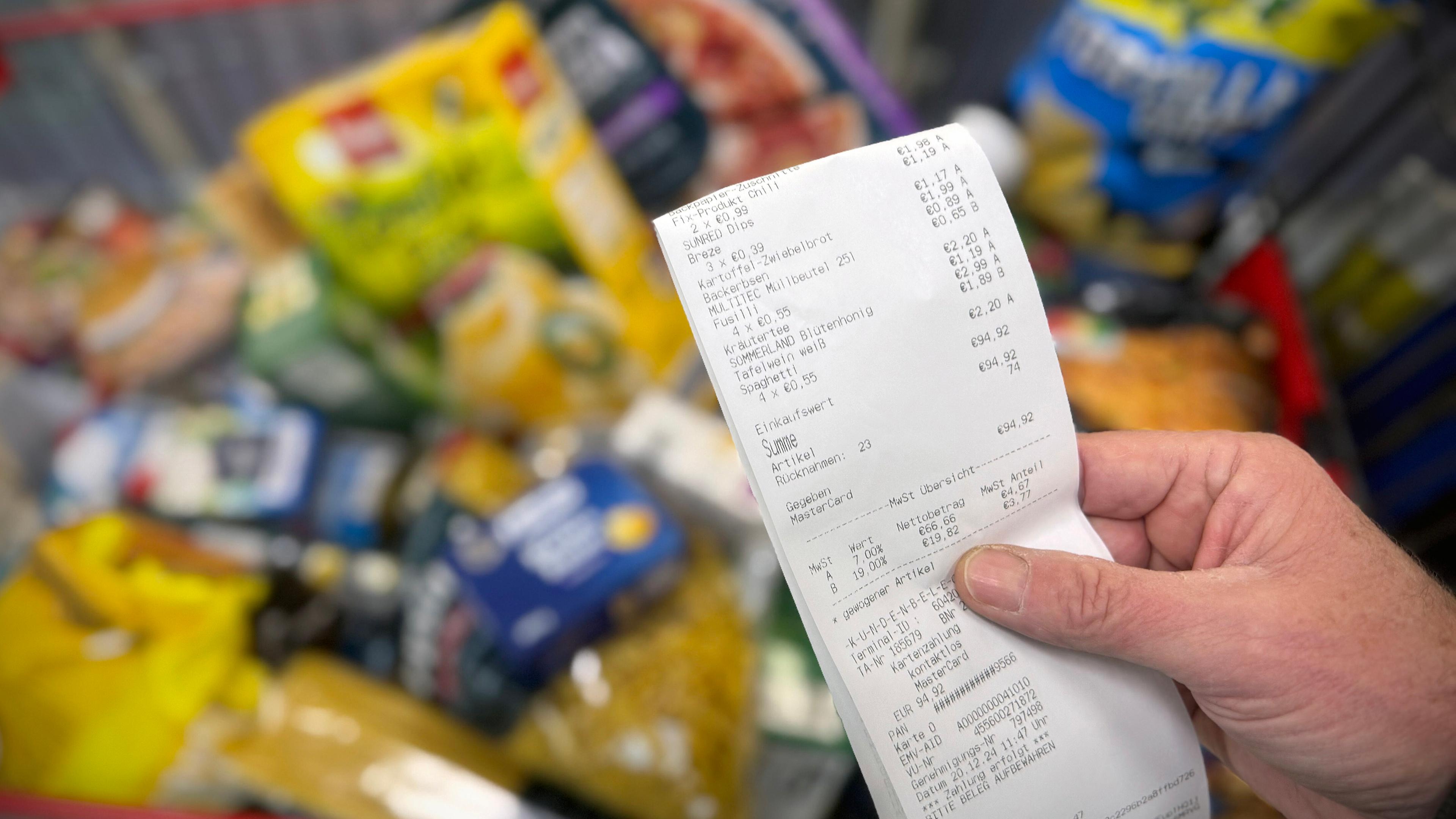 Eine Hand hält einen Kassenbon und Lebensmittel im Einkaufswagen