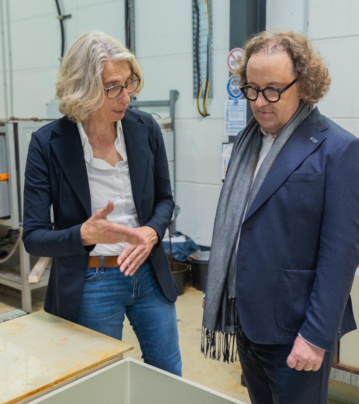 Das Geschäftsführungsduo des Stahlverzinkungsunternehmens Zinq, Birgitt Bendiek und Lars Baumgürtel steht in einer Werkshalle.