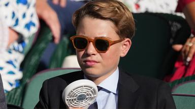 Ein Junge trägt eine Sonnenbrille, einen Anzug und erfrischt sich mit einem Ventilator.
