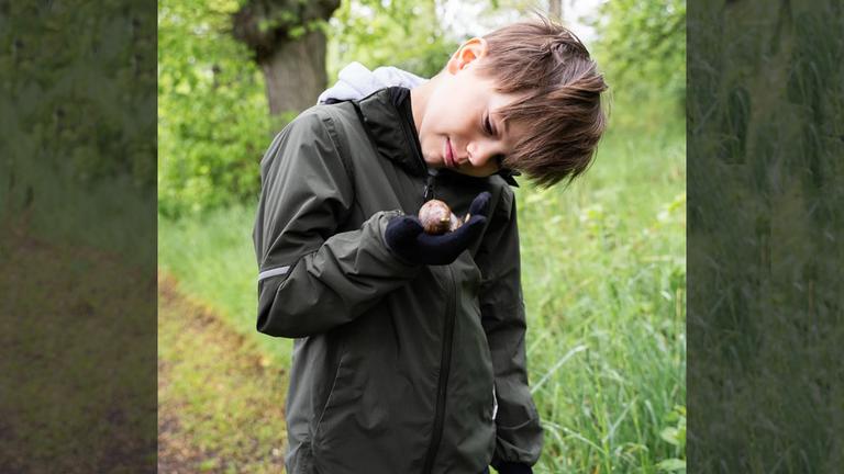 Am Tag der biologischen Vielfältigkeit hat es Prinz Oscar ins Grüne verschlagen. Mit großen Augen inspiziert der 9-Jährige eine Schnecke, die ihm über den Weg geschlichen ist. (23.05.2025) 