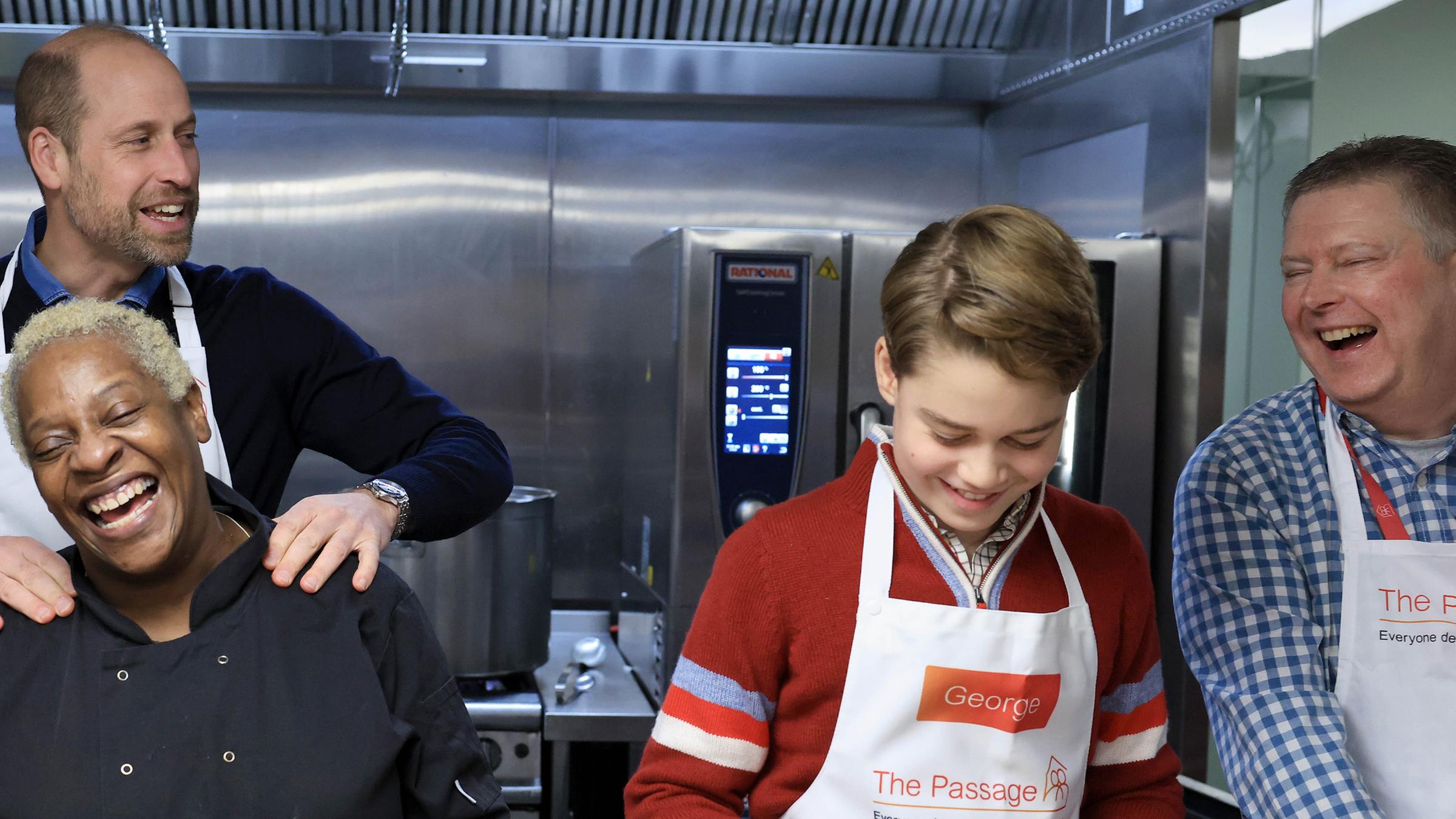 Der Prinz von Wales und Prinz George in der Küche von „The Passage“ mit Küchenchefin Claudette und dem Geschäftsführer von „The Passage“, Mick Clarke, während sie beim Zubereiten des Weihnachtsessens helfen.