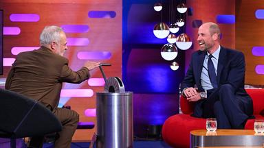 Prinz William sitzt auf einem roten Sofa und lächelt zum Moderator. 
