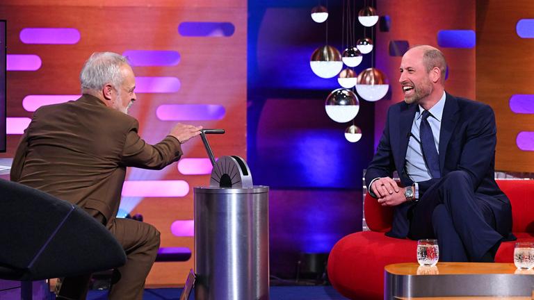Prinz William sitzt auf einem roten Sofa und lächelt zum Moderator. 