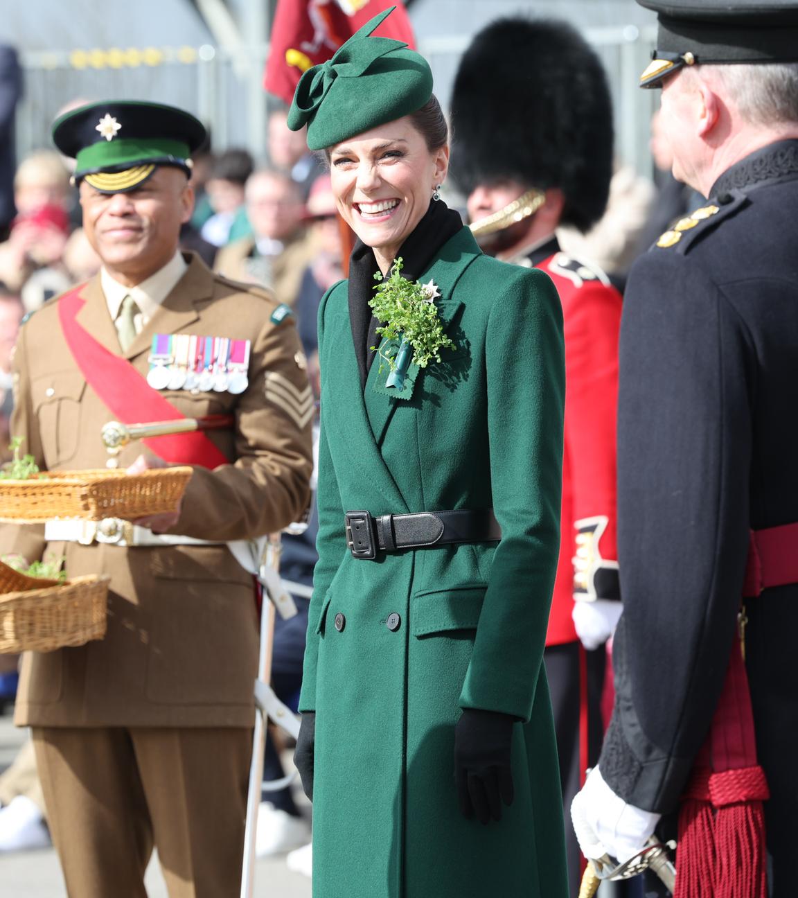 Prinzessin Kate bei der St. Patrick's Day Parade. Sie trägt ein grünes Kleid und lächelt breit. Um sie herum stehen Soldaten.
