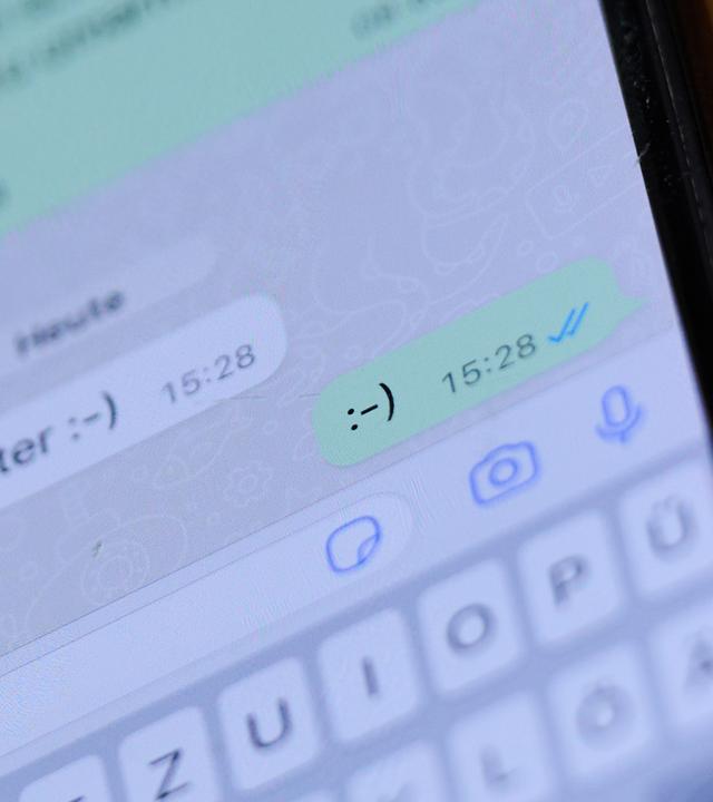 Illustration - Ein Smiley ist in einem Chat auf einem Handydisplay zu sehen.