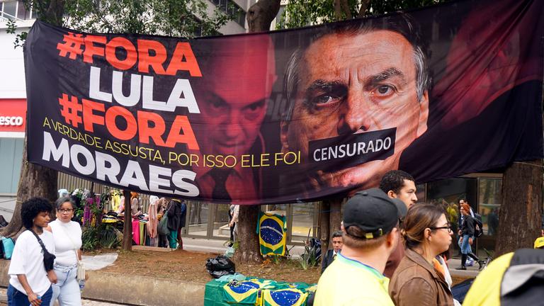Eine Demonstration in Sao Paulo. Es wurde ein großes Plakat aufgehangen auf dem der ehemalige Präsident Bolsonaro abgebildet ist. Sein Mund wurde zugeklebt.
