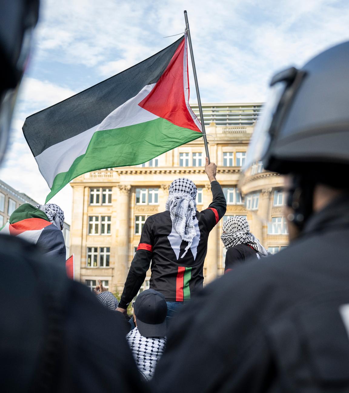 14.10.2023, Hessen, Frankfurt/Main: Ein Teilnehmer einer Pro-Palästina Demonstration schwenkt eine Palästina-Flagge, während Polizisten die Situation beobachten.