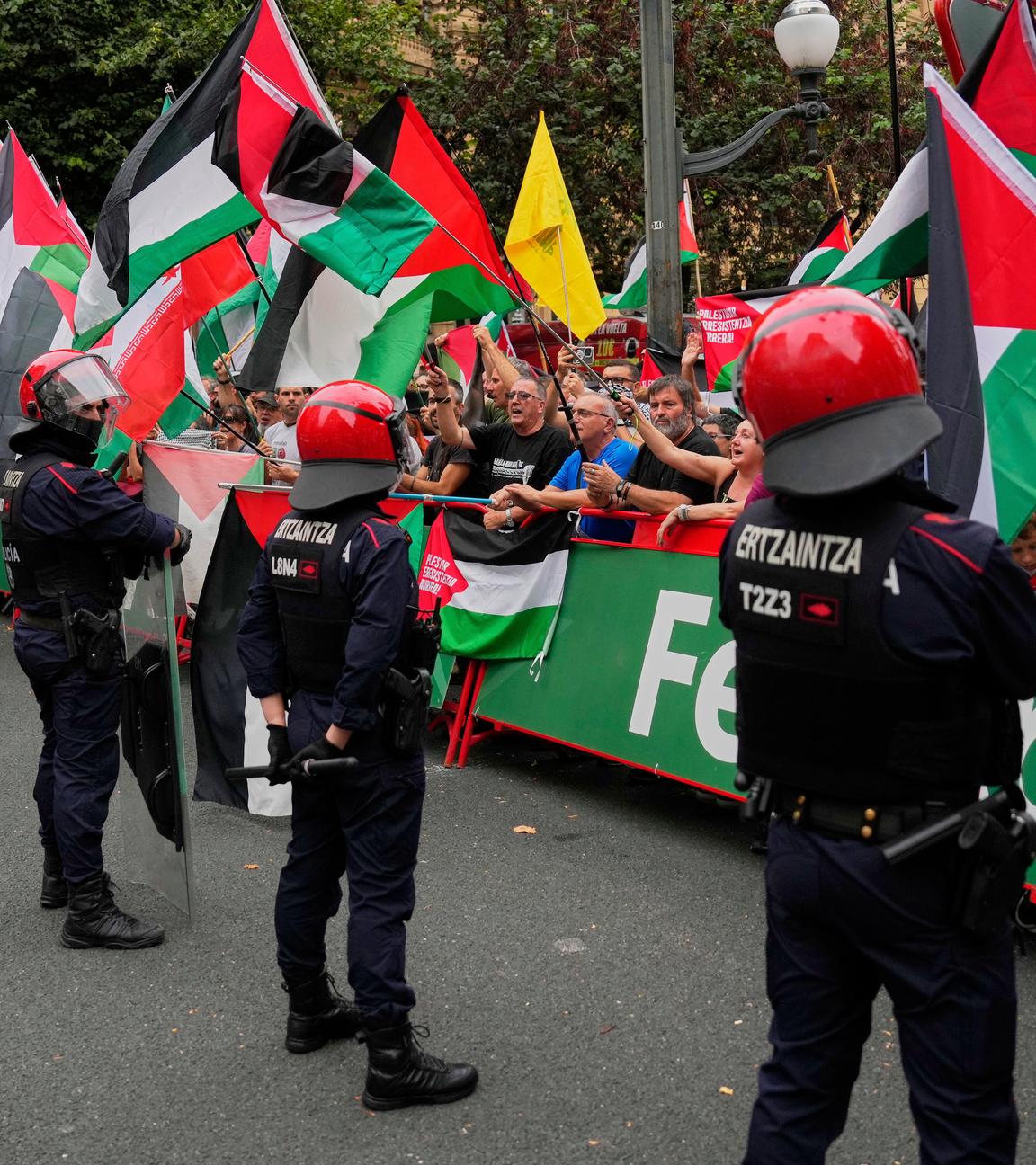 Personen, die hinter der Absperrung stehen, halten im Zielbereich der 11. Vuelta-Etappe Palästina-Flaggen über die Strecke. Davor stehen Polizisten.
