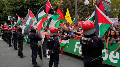Personen, die hinter der Absperrung stehen, halten im Zielbereich der 11. Vuelta-Etappe Palästina-Flaggen über die Strecke. Davor stehen Polizisten.