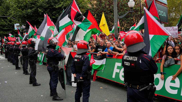 Personen, die hinter der Absperrung stehen, halten im Zielbereich der 11. Vuelta-Etappe Palästina-Flaggen über die Strecke. Davor stehen Polizisten.