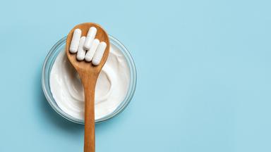 Probiotische Kapseln und eine Schale Joghurt auf blauem Untergrund.