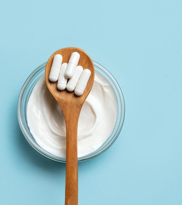 Probiotische Kapseln und eine Schale Joghurt auf blauem Untergrund.