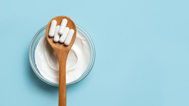 Probiotische Kapseln und eine Schale Joghurt auf blauem Untergrund.