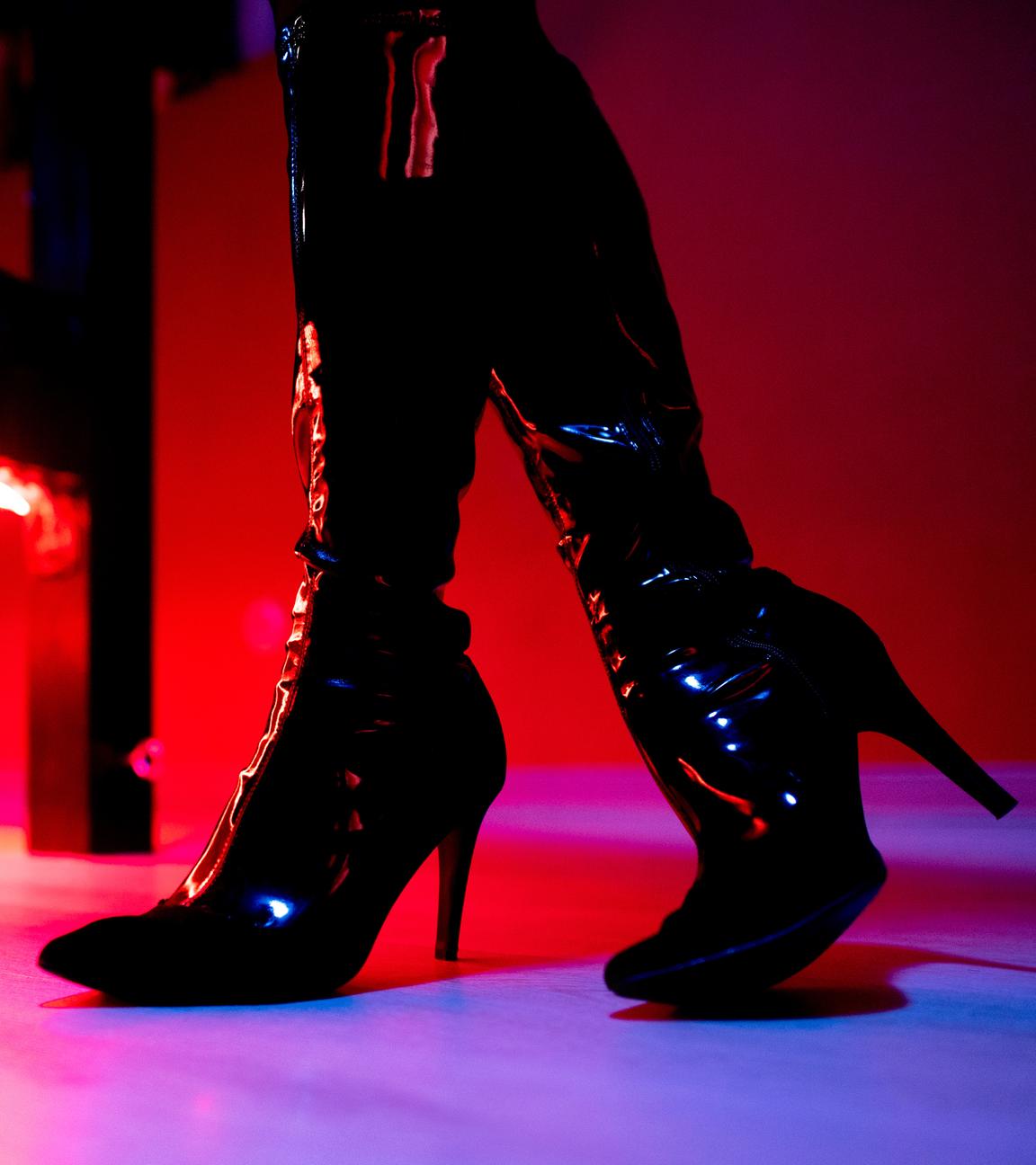 Die Beine eine Prostituierten in schwarzen Stiefeln vor der roten Beleuchtung unter einem Bett in einem Studio.