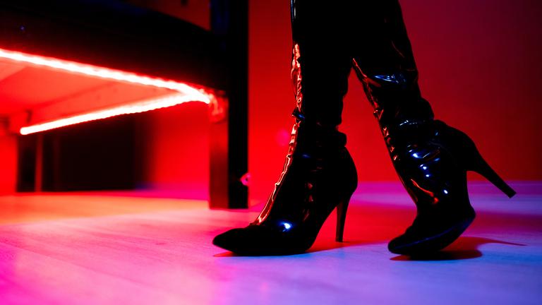 Die Beine eine Prostituierten in schwarzen Stiefeln vor der roten Beleuchtung unter einem Bett in einem Studio.