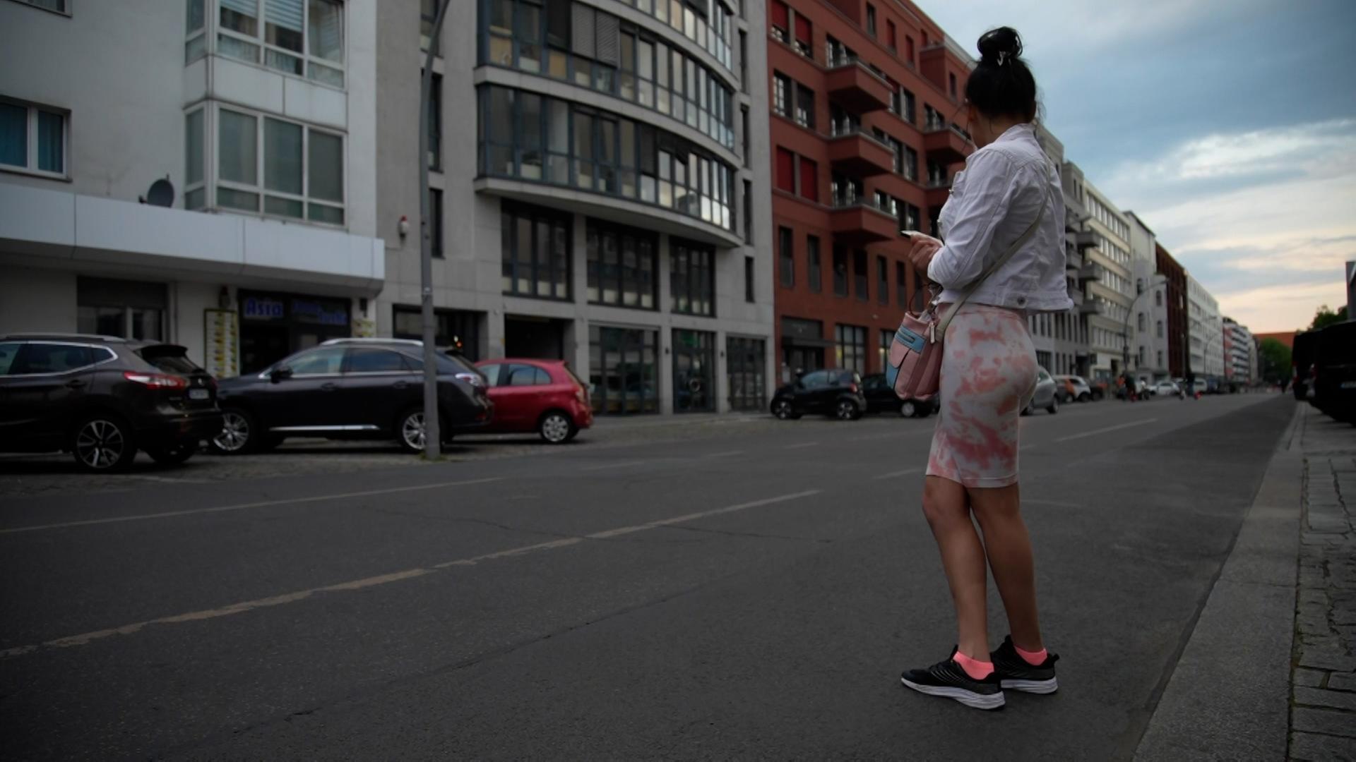 Eine Frau steht knapp bekleidet am Straßenrand.