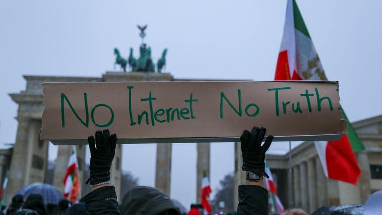 Exil-Iraner protestieren vor dem Brandenburger Tor gegen das islamische Regime im Iran. Im Vordergrund ist ein Schild mit der Aufschrift "No Internet, No Truth" zu sehen.