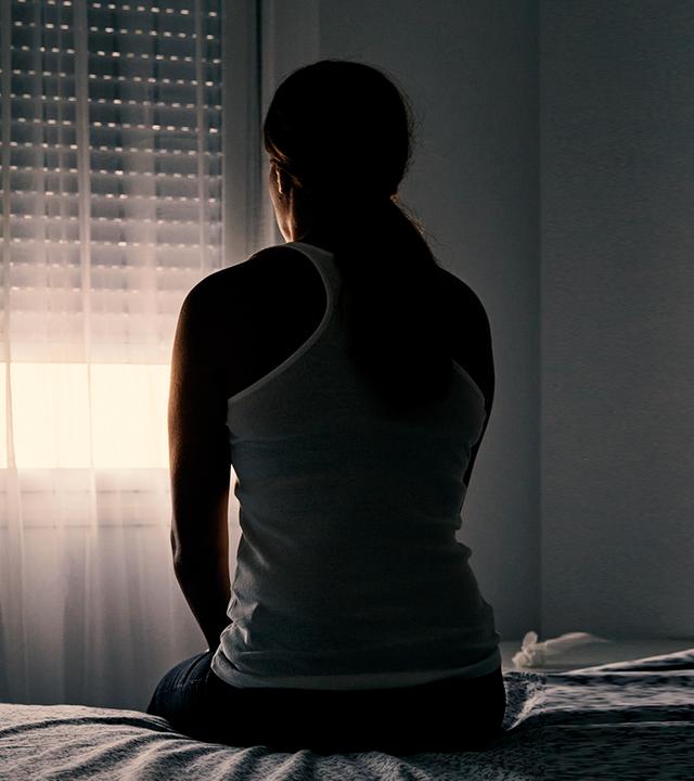 Eine Frau sitzt auf einem Bett in einem dunklen Raum