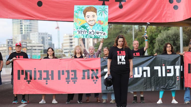 Regierungsgegner halten um 6:29 Uhr morgens eine Schweigeminute für die Opfer der von der Hamas angeführten Angriffe vom 7. Oktober ab; dabei halten sie ein großes Transparent mit der Aufschrift „Das Volk wird sich an seine Söhne und Töchter erinnern“ und blockieren eine Hauptverkehrsstraße in Tel Aviv