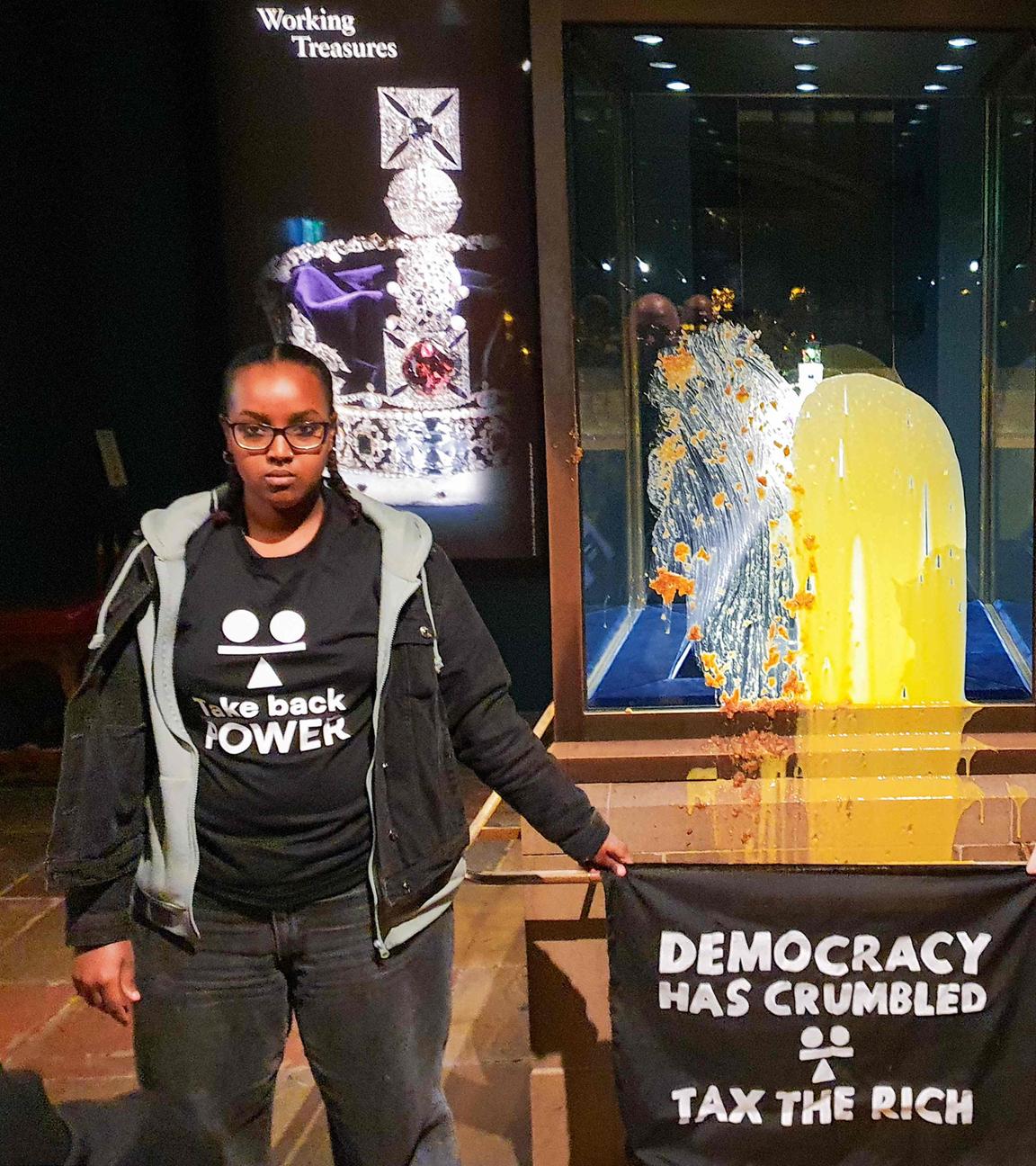Ein Foto vom 06.12.2025 zeigt Anhänger der zivilen Widerstandsgruppe "Take Back Power" mit einem Banner mit der Aufschrift "Democracy has crumbled – Tax The Rich", nachdem sie Dessert und Vanillesoße über die Vitrine mit den Kronjuwelen im Tower of London geschüttet hatten.