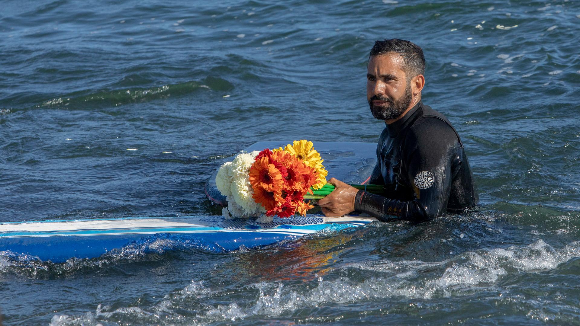 Ein Mann hält Blumen während einer Gedenkfeier für drei vermisste Surfer in Ensenada, Mexiko
