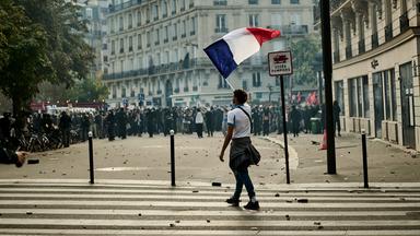 Während Protesten in Paris läuft eine Person mit einer Frankreich-Flagge über eine Straße.