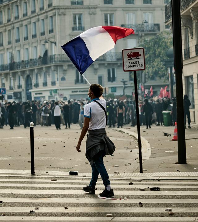 Während Protesten in Paris läuft eine Person mit einer Frankreich-Flagge über eine Straße.