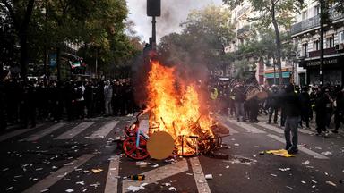 Ein Demonstrant wirft am 17. Oktober 2026 bei einer Protestaktion gegen die hohen Lebenshaltungskosten in Paris einen Stuhl ins Feuer.