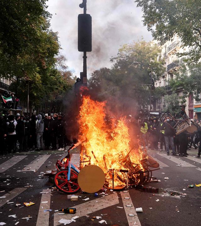 Ein Demonstrant wirft am 17. Oktober 2026 bei einer Protestaktion gegen die hohen Lebenshaltungskosten in Paris einen Stuhl ins Feuer.