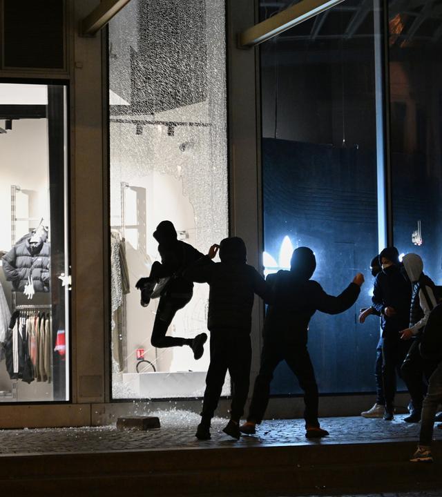 Jugendliche zerschlagen im Zuge der Proteste in Paris am Abend eine Schaufensterscheibe.