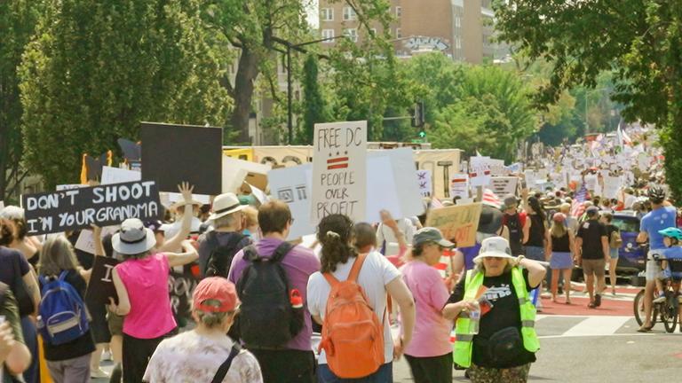 Demonstranten laufen in einer von Bäumen gesäumten Straße und entfernen sich von der Kamera.