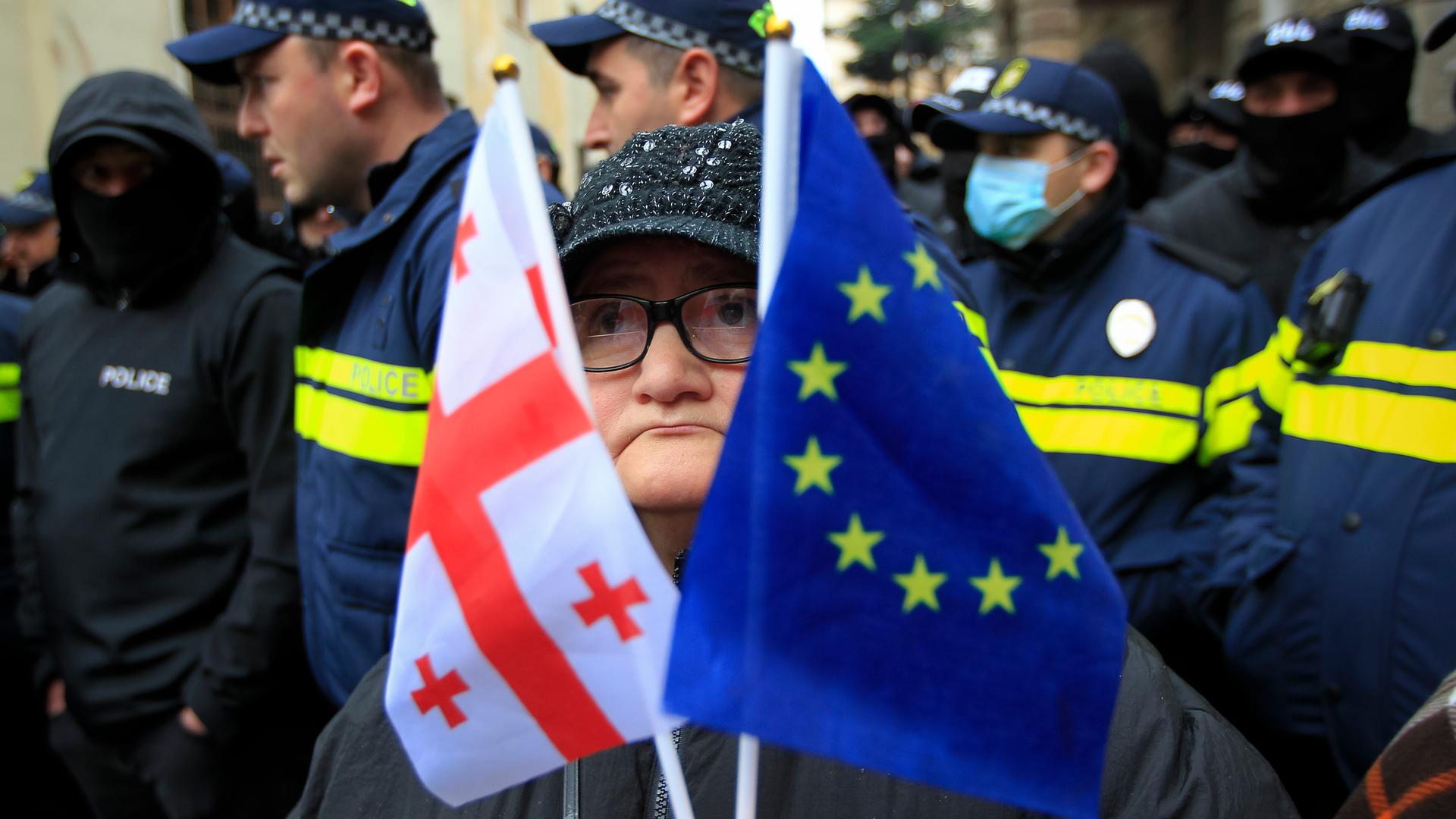 Eine Frau mit einer EU- und einer georgischen Nationalflagge steht vor der Polizei.