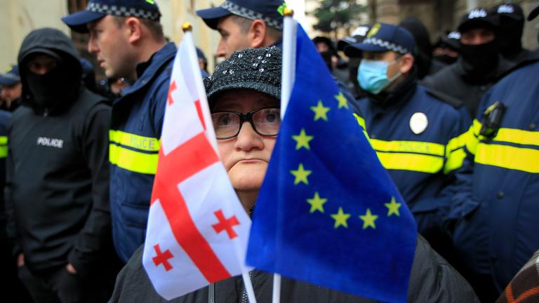 Eine Frau mit einer EU- und einer georgischen Nationalflagge steht vor der Polizei.