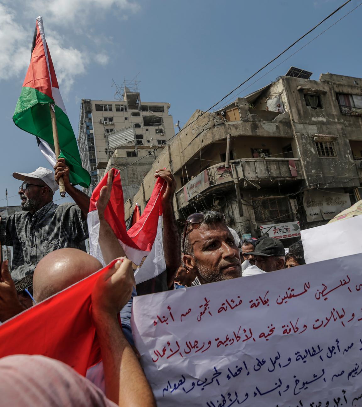 proteste in Gaza-Stadt.Die Menschen halten palästinensische Flaggen in die Luft. Im Hintergrund stehen verwahrloste Gebäude.