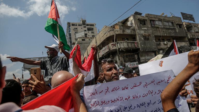proteste in Gaza-Stadt.Die Menschen halten palästinensische Flaggen in die Luft. Im Hintergrund stehen verwahrloste Gebäude.