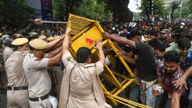 Demonstrierende stehen neben einem beschädigten Polizeibus nach Ausschreitungen bei einer Protestkundgebung in Neu-Delhi.